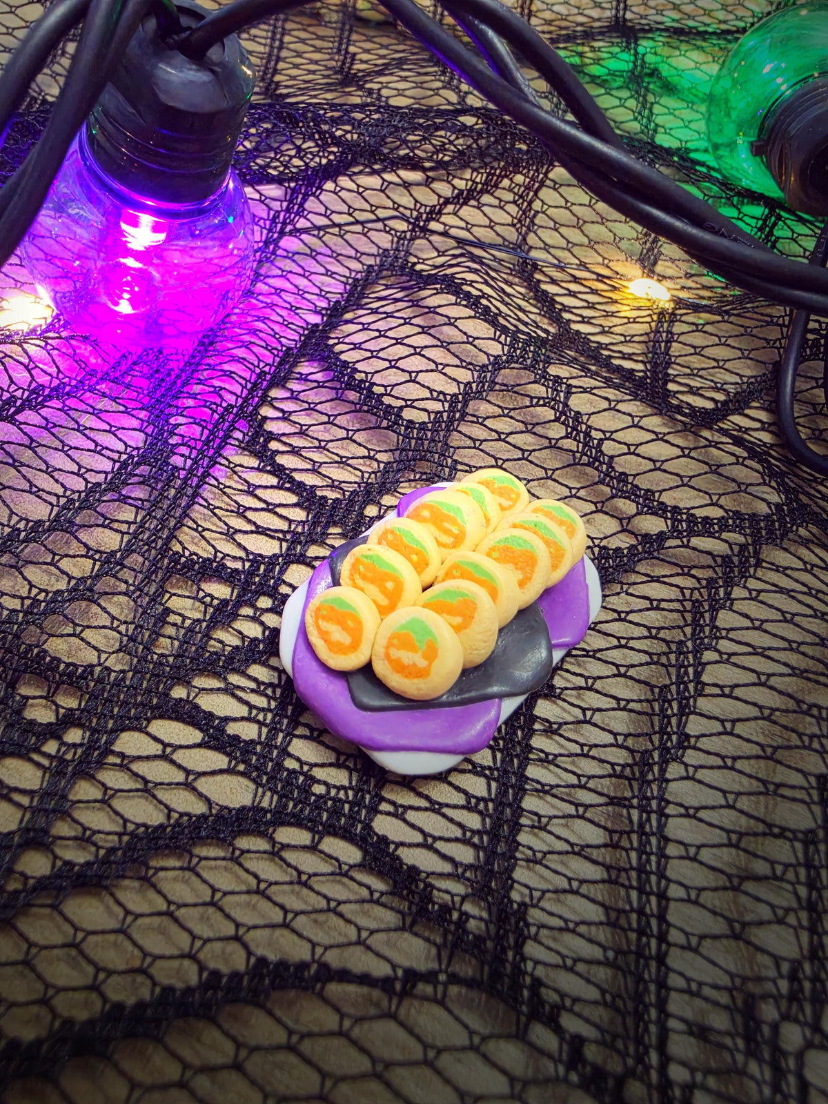 Miniature pumpkin cookie platter styled on spiderweb lace with glowing Halloween lights