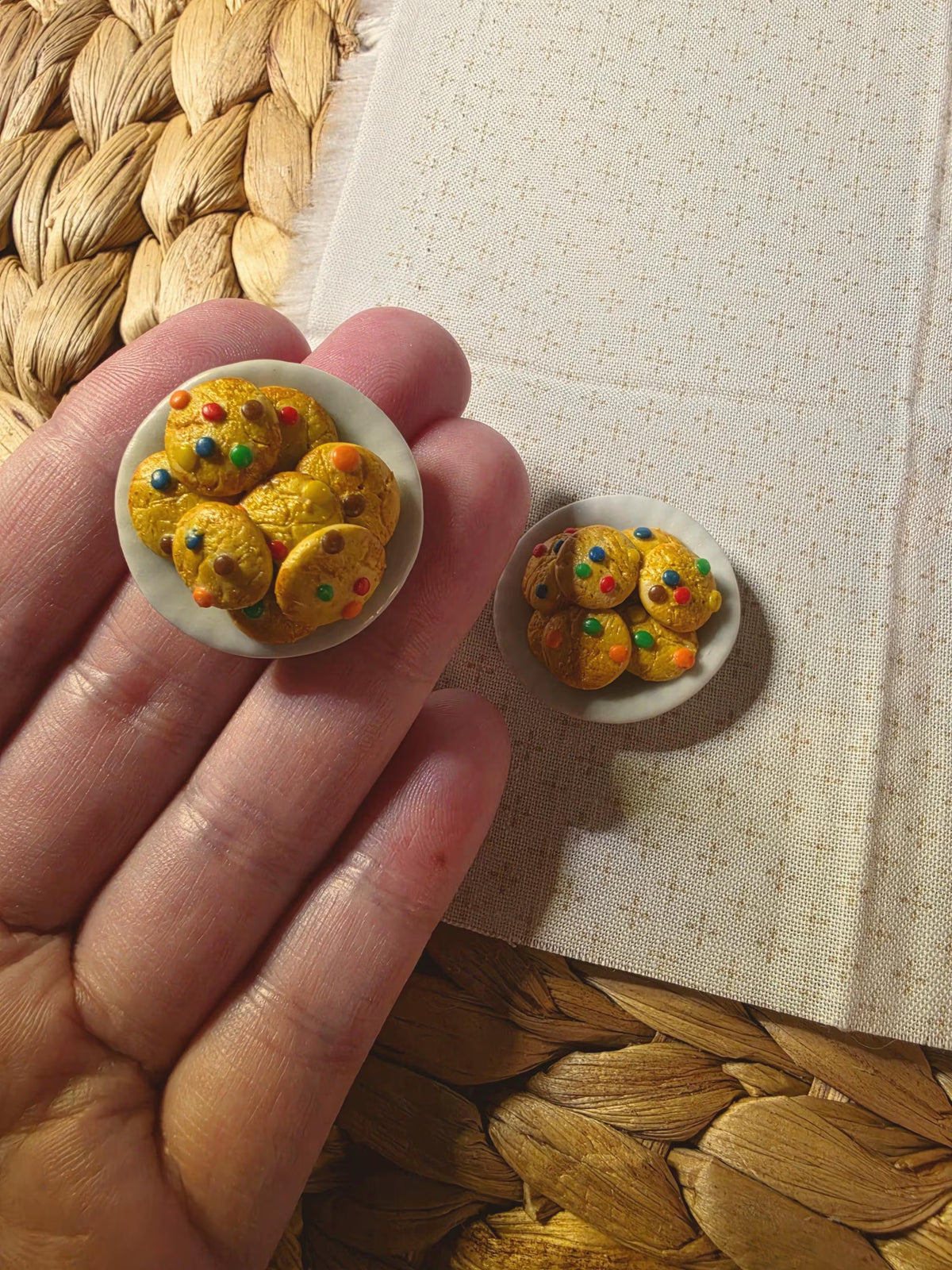 Hand holding a tiny candy-topped cookie plate to show its miniature size, about 1 inch across