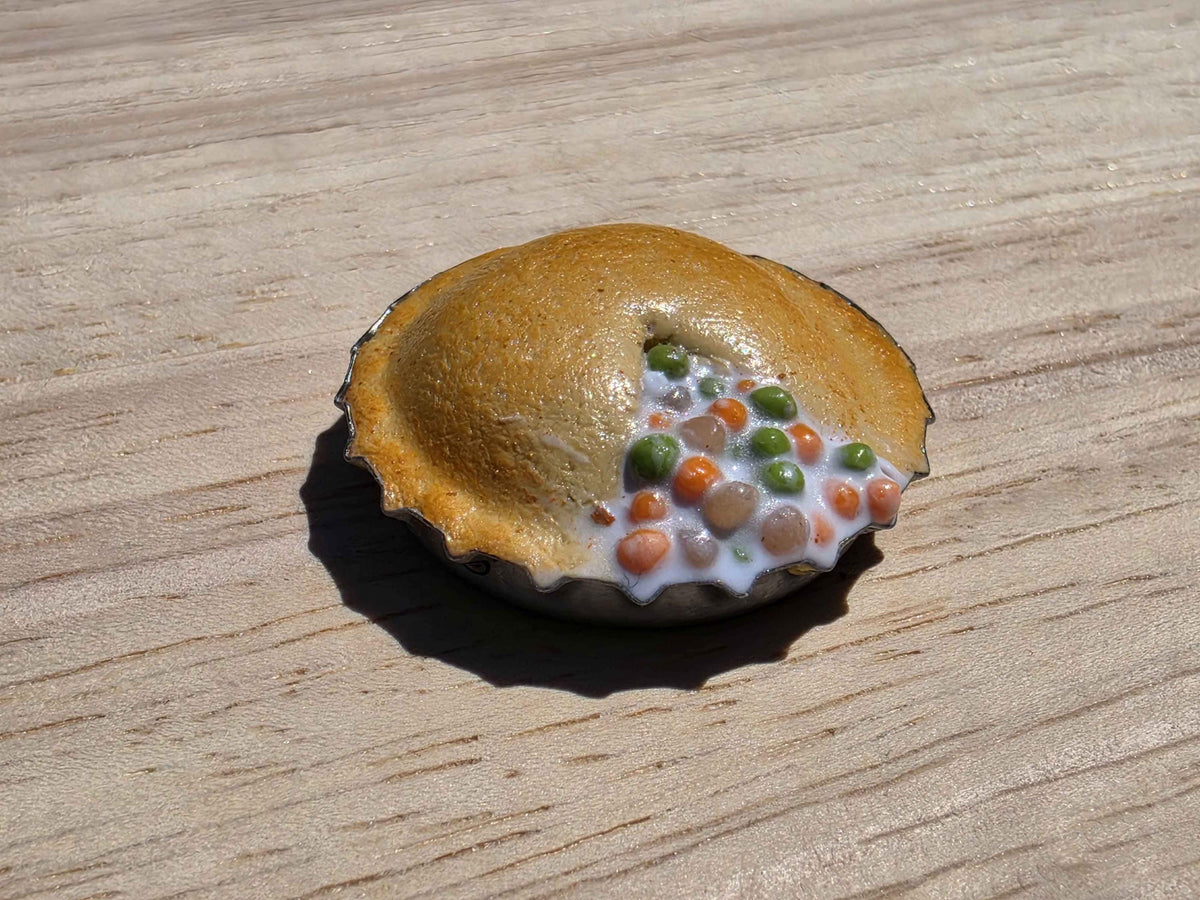 Mini pot pie magnet with a golden crust and peas and carrots peeking out, handmade from polymer clay