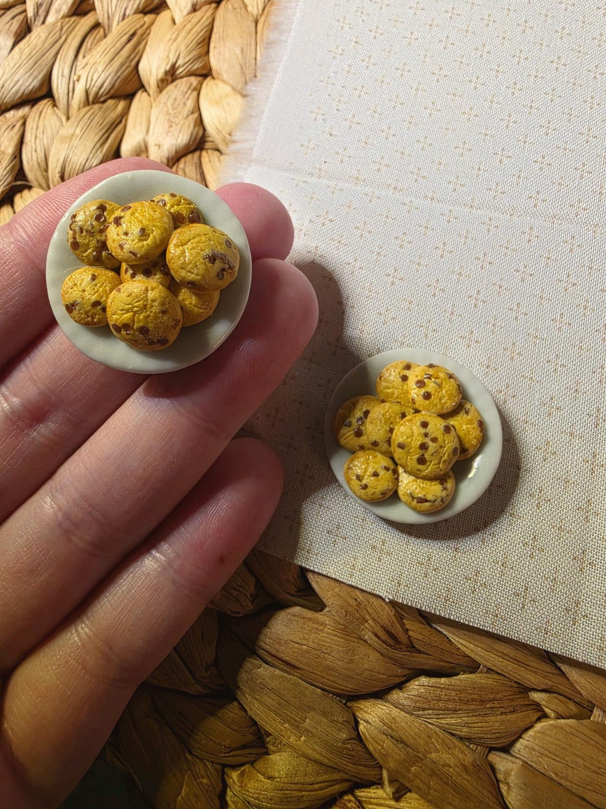 Hand holding a tiny chocolate chip cookie plate to show its miniature size, about 1 inch across